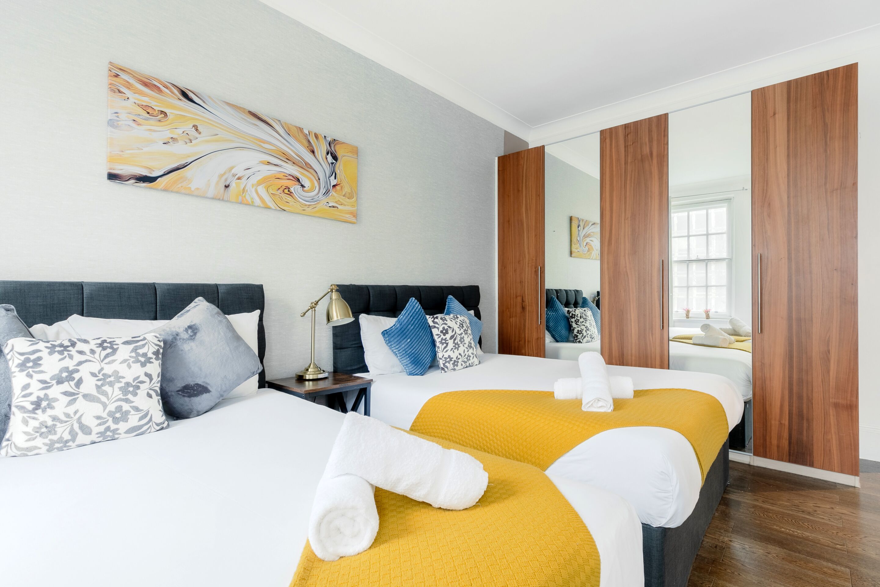 A hotel room with two beds, a nightstand, a lamp, and a large mirror.