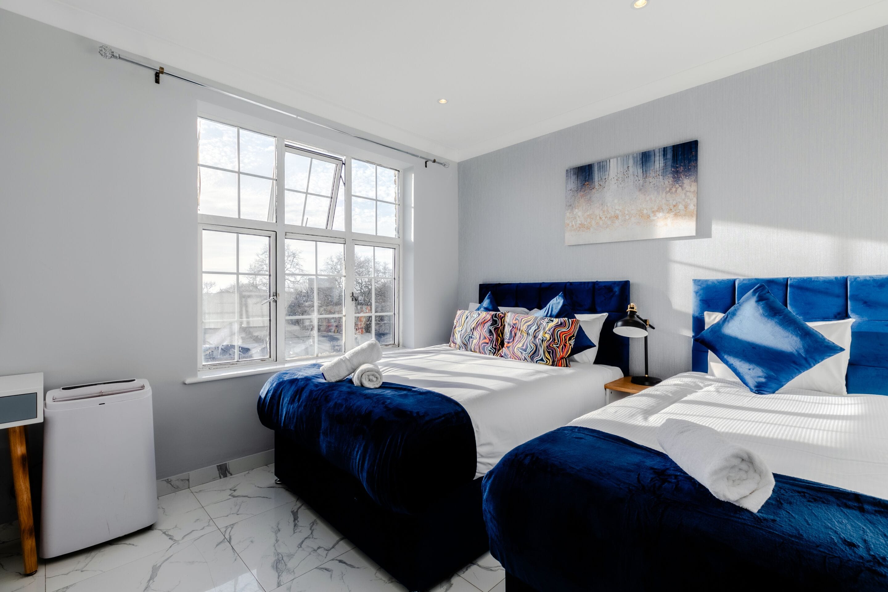 Een hotelkamer met twee bedden, een groot raam, een schilderij aan de muur en een klein tafeltje.