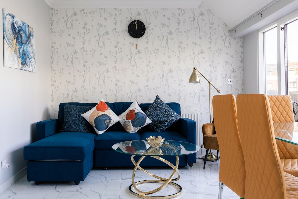 Una sala de estar moderna con un sofá azul, una mesa de centro de vidrio y un ventanal grande.