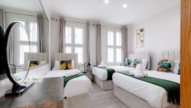 A hotel room with two beds, a desk with a mirror, and a window with curtains. - Marble Arch Apartments (London)