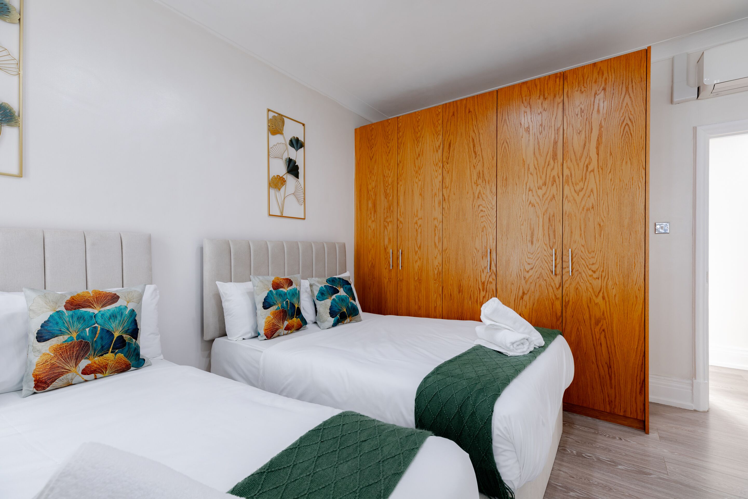 A hotel room with two beds, a wooden wardrobe, and a framed artwork on the wall.