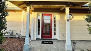 A two-story house with a red door, a porch with columns, and a welcome mat.