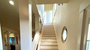 A staircase with wooden steps and white walls, leading to a landing with a view of a kitchen area.