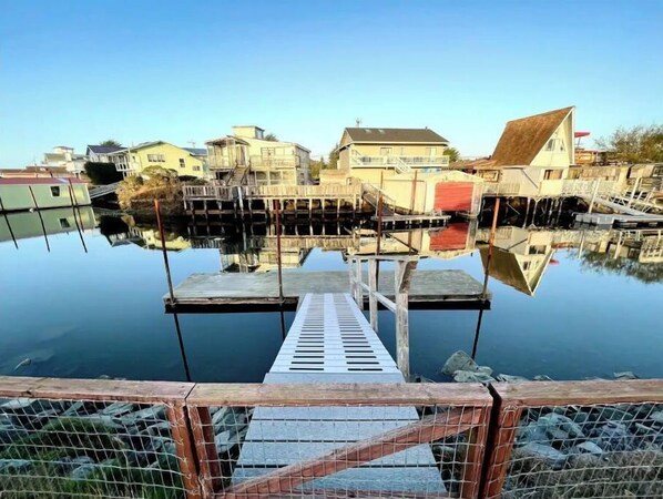 A calm waterfront with a wooden dock leading into a clear body of water, surrounded by residential buildings.