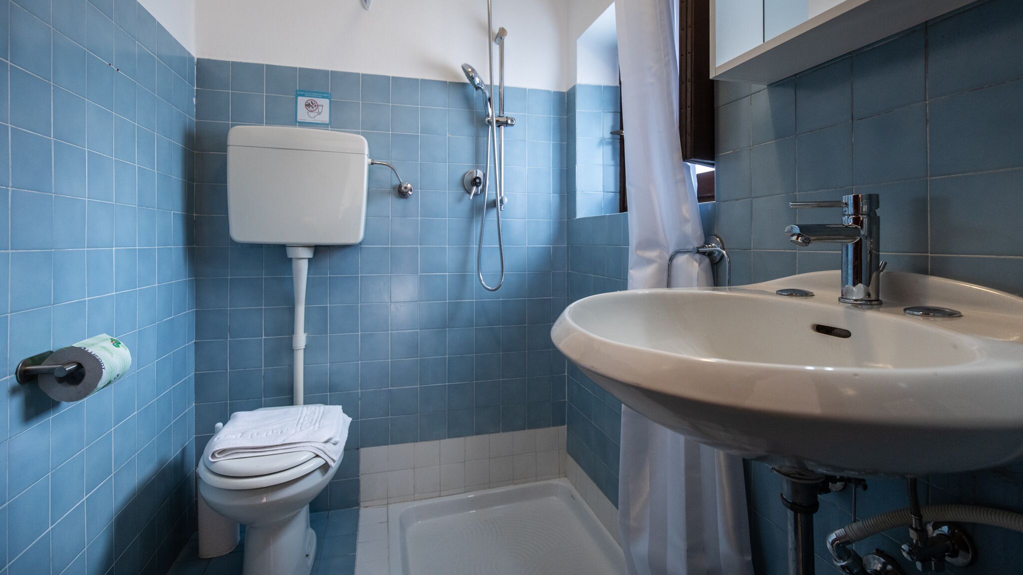 Ein Badezimmer mit Toilette, Waschbecken, Dusche und einer blau gefliesten Wand.