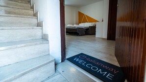 A staircase leading to a room with a bed, a sofa, and a wooden floor. A welcome mat with "Italianway" and "WELCOME" is visible. - Italianway - Castellana Mono 68 (Udine)