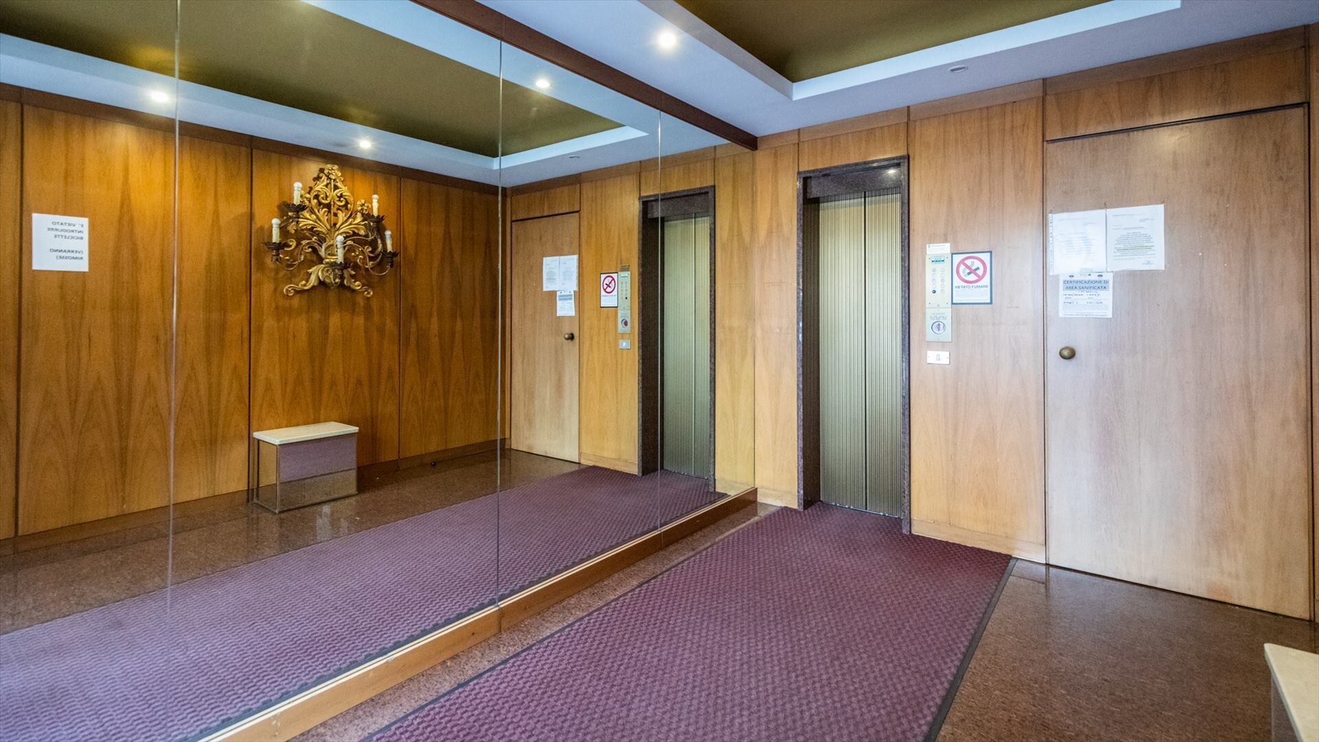 Una hall d'albergo con pannelli di legno, una panca, un ascensore e un pavimento tappezzato.