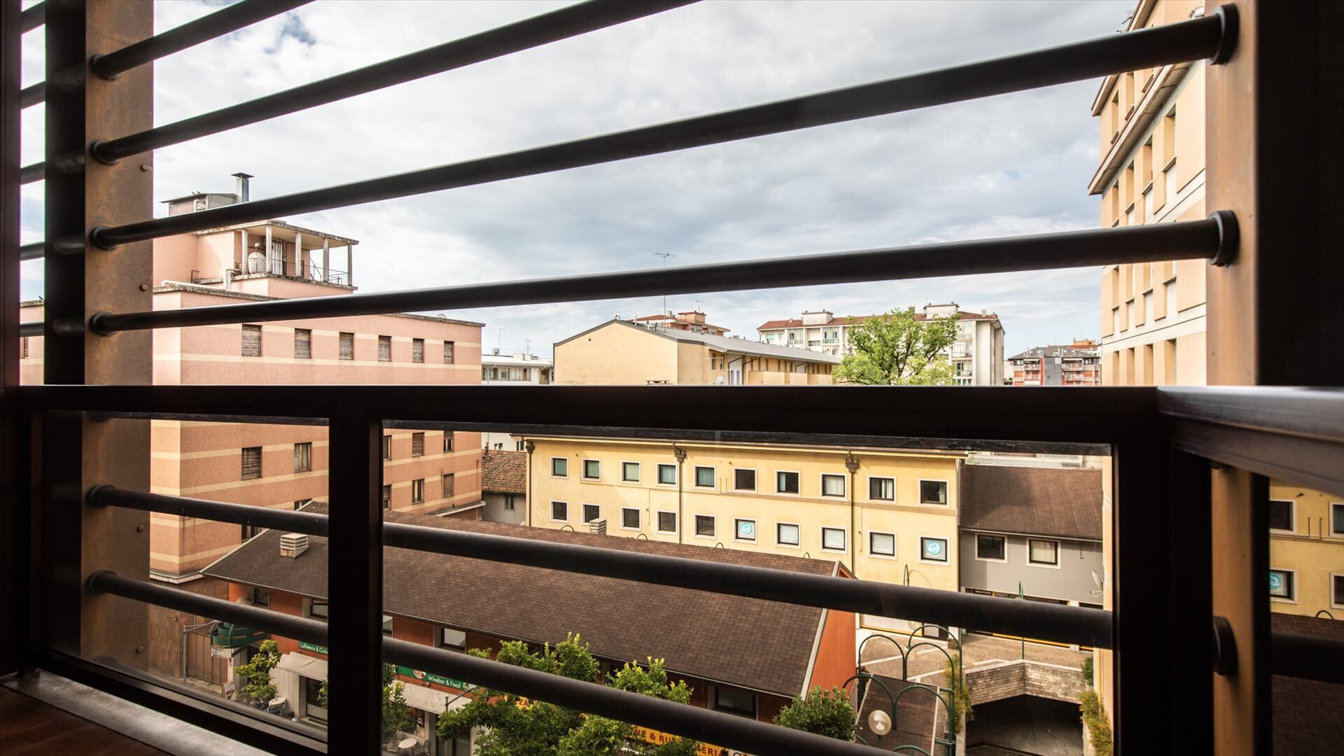 A view through metal bars of a cityscape with buildings, including a yellow building with multiple windows and balconies.