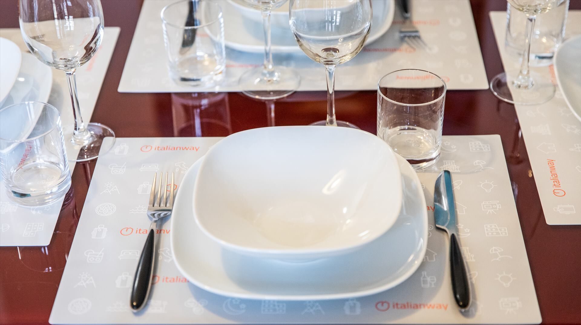 Una mesa con un plato blanco, un cuchillo y un tenedor sobre un mantel individual con el logotipo de Italianway.