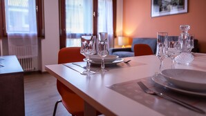 A dining table set with clear glassware and plates, a fork, and a knife, with a chair and a sofa in the background. - Italianway - Aquileia 53 (Udine)