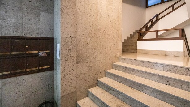 A staircase with a wooden handrail and beige steps, leading to a landing with a wall-mounted mailbox. - Italianway - Aquileia 53 (Udine)