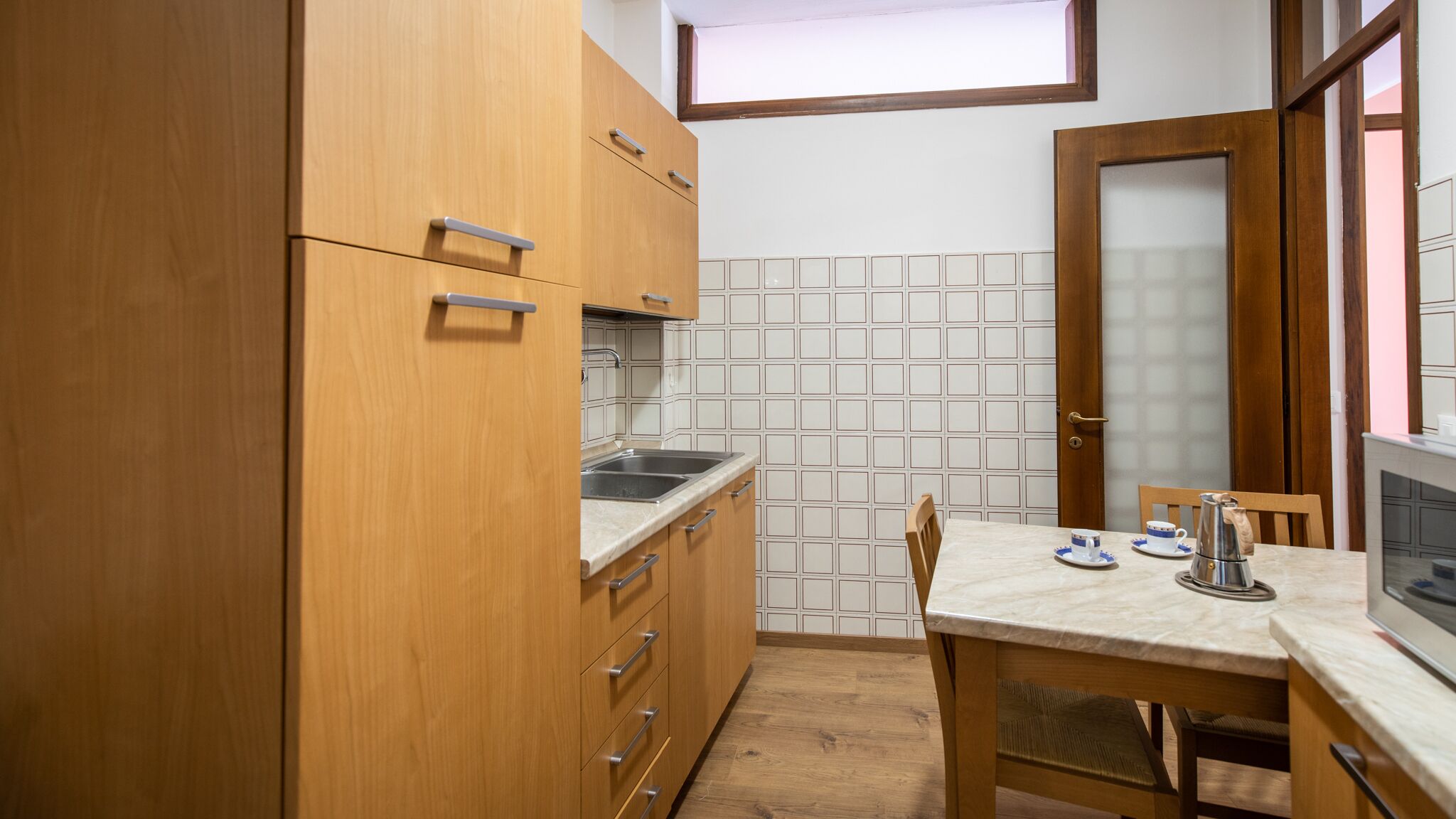 A compact kitchen with wooden cabinets, a sink, a tiled backsplash, and a dining table with chairs.
