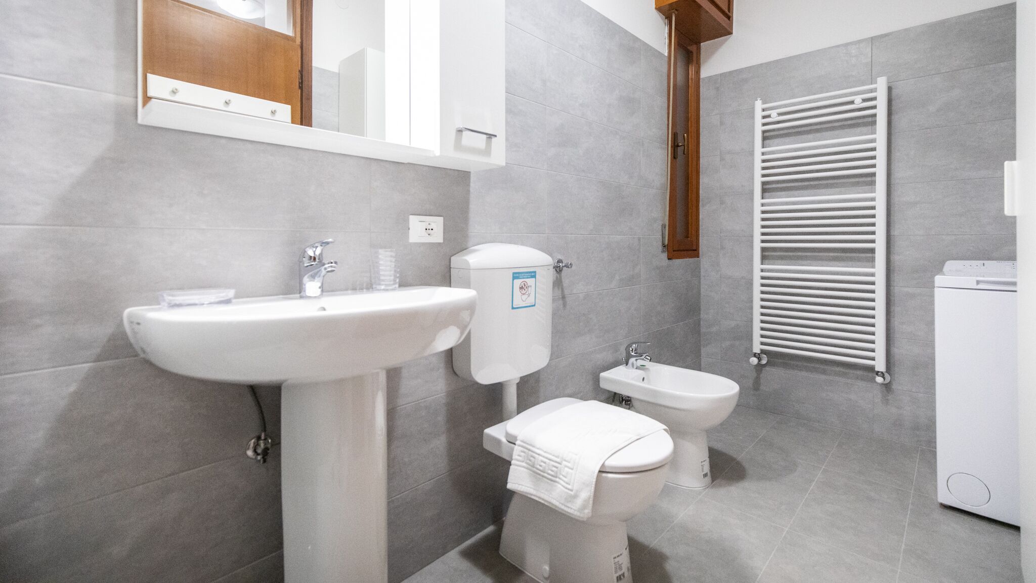 A modern bathroom with a large sink, a toilet, a bidet, and a towel rack.