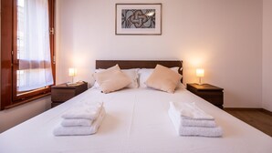 A neatly made bed with white linens and two towels folded at the foot. There are two bedside tables with lamps, and a framed artwork hangs above the bed. - Italianway - Aquileia 53 (Udine)