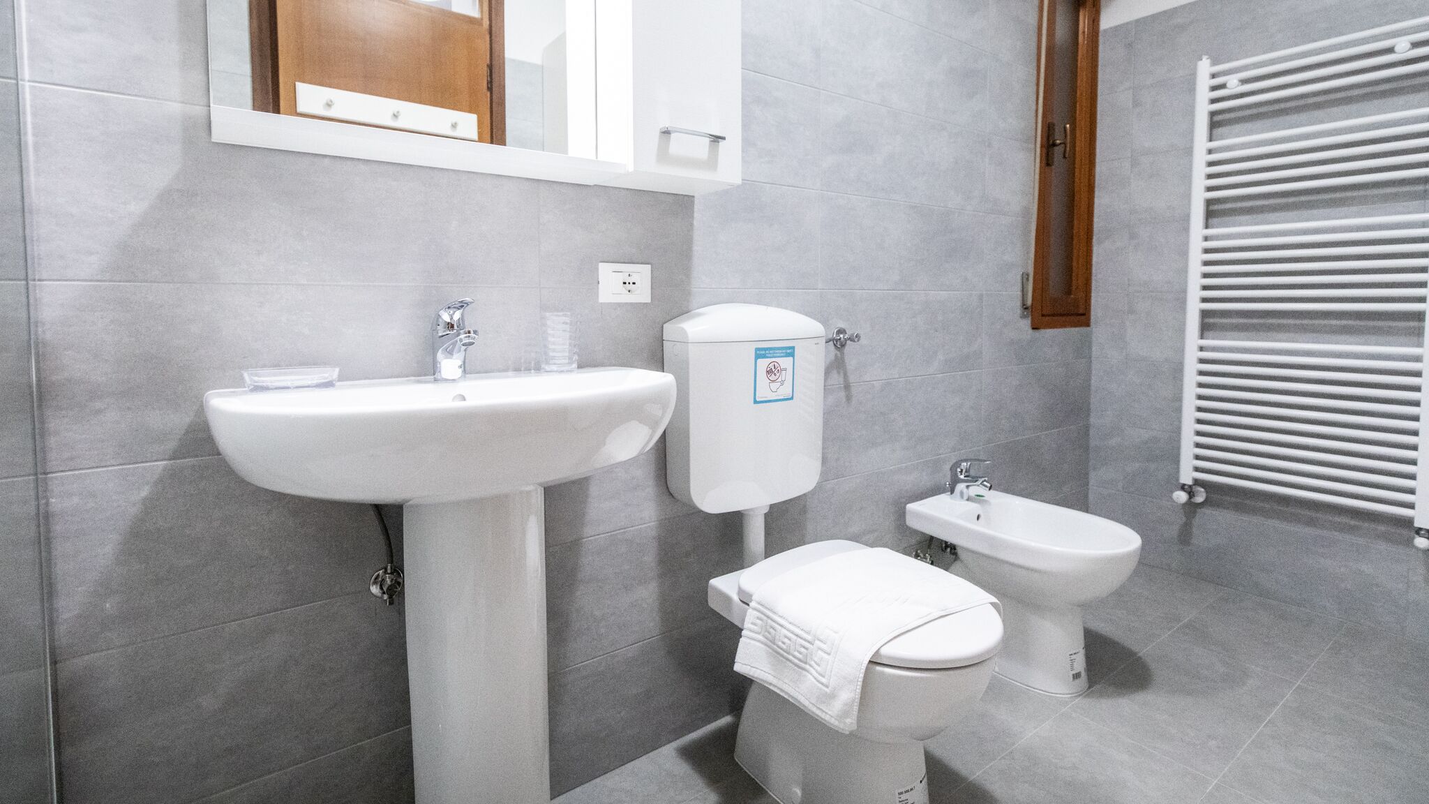 A modern bathroom with a pedestal sink, toilet, bidet, and a towel rack.