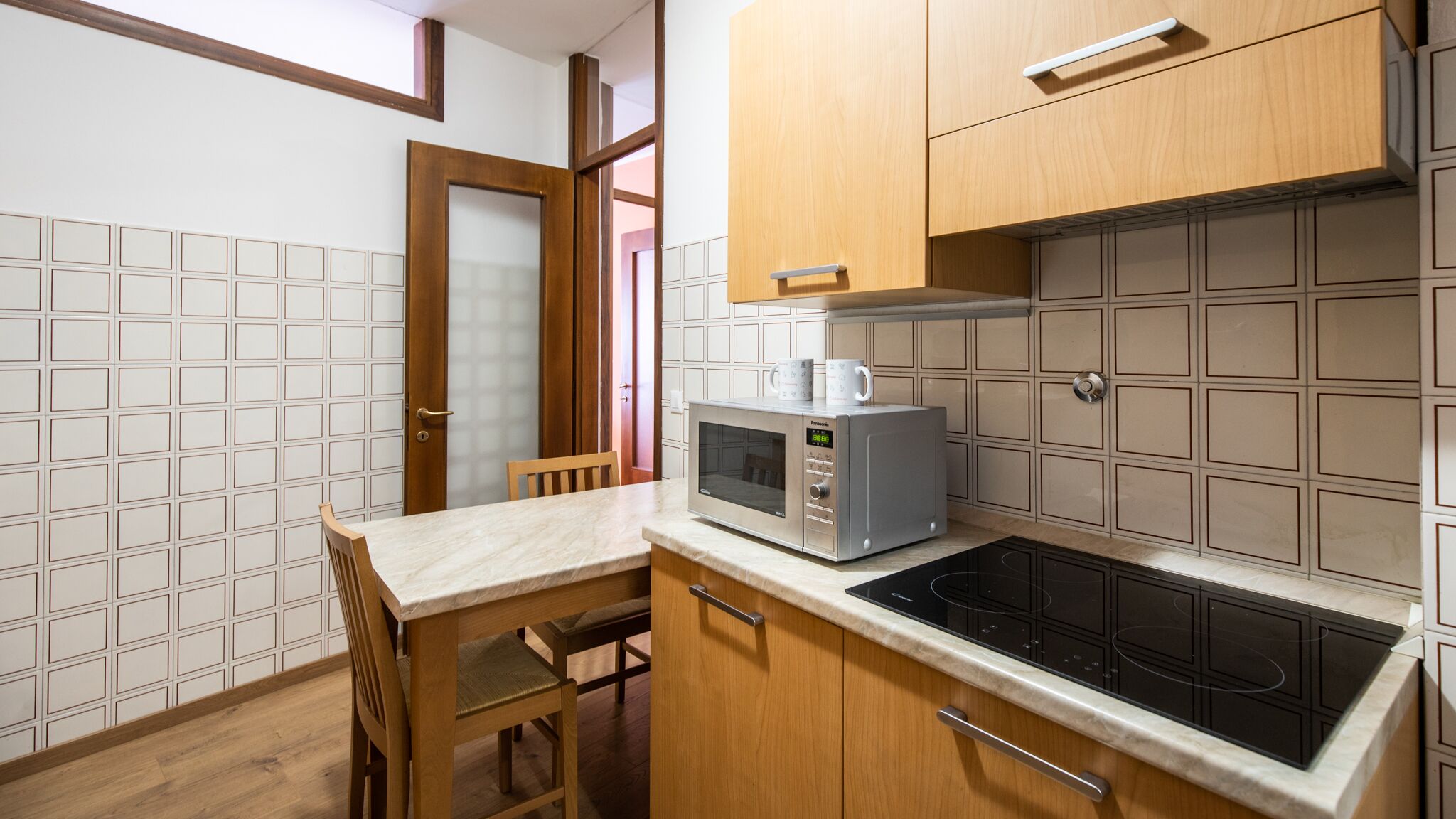 A compact kitchen with a microwave, a stove, and a dining area with a chair.