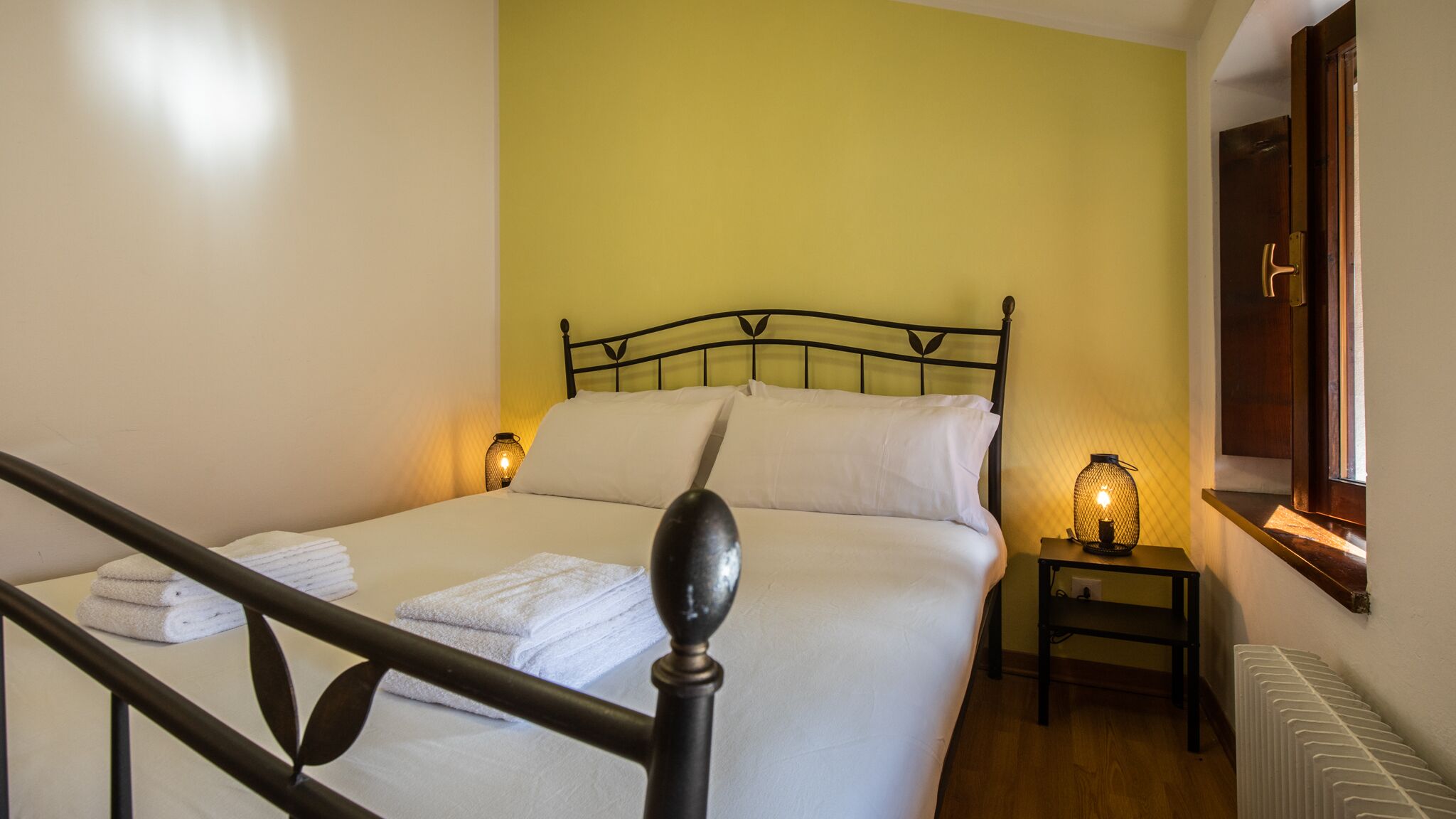 A neatly made bed with white linens, two bedside lamps, and a radiator.