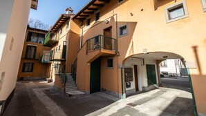 A narrow street with a building featuring a green balcony and a door with a metal gate. - Italianway - Castellana 68 (Udine)
