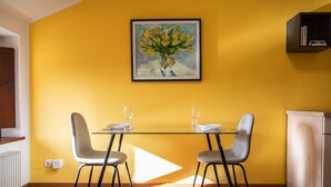 A dining area with a glass table, two grey chairs, and a painting of flowers on the wall. - Italianway - Castellana 68 (Udine)