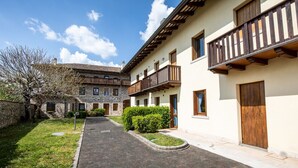 A courtyard with a paved path, stone buildings with wooden balconies, and a tree with bare branches. - Italianway - Galilei 41 (Udine)