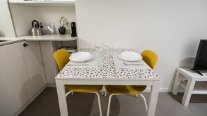 A compact dining area with a white table, yellow chairs, and a small TV on a white stand. - Italianway - Del Sale 4 (Udine)