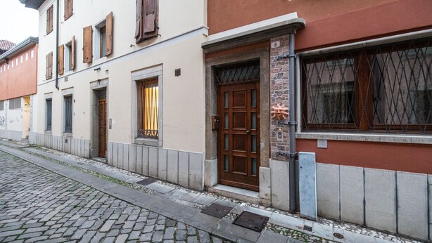 A building with a cobblestone street, a wooden door, and a window with a metal grille. - Italianway - Del Sale 4 (Udine)