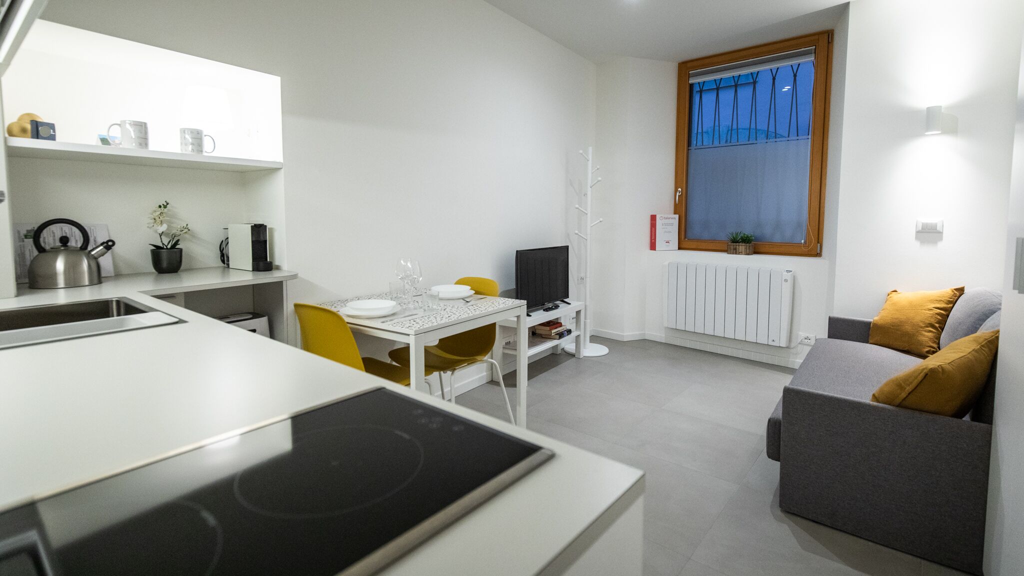 A compact kitchen with a dining area, a sofa, and a window with blinds.