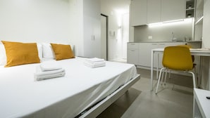 A modern hotel room with a bed, a desk, and a chair. There is a kitchen area with cabinets and a countertop. - Italianway - Del Sale 4 (Udine)