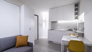 A modern, compact kitchen with white cabinetry, a dining table, and a sofa with a mustard-colored pillow. - Italianway - Del Sale 4 (Udine)