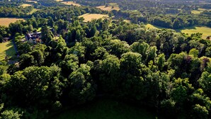 Luchtbeeld van een landelijk gebied met een groot landhuis, omgeven door dichte bossen en glooiende heuvels.