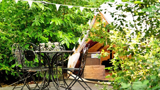 An outdoor dining area with a metal table and chairs, surrounded by lush greenery. - Bedouin Bell Tent (Woolton Hill)