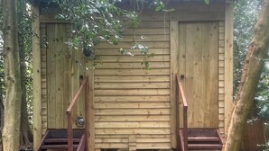 A wooden shed with two sets of stairs leading up to a door, surrounded by trees and covered with leaves.
