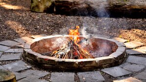 A circular stone fire pit with burning logs and smoke rising.