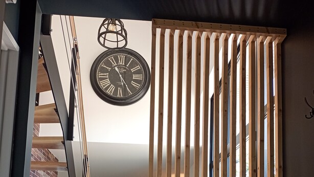 Ein modernes Interieur mit einer Holzhakepartition, einer Wanduhr und einer Treppe, die in eine obere Ebene führt.