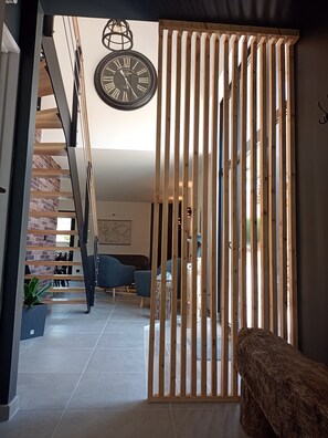 A modern interior with a wooden slat partition, a hanging wall clock, and a staircase leading to an upper level.
