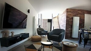 Ein modernes Wohnzimmer mit einem großen Flachbildfernseher, zwei Sesseln, einem Couchtisch und einem gemusterten Teppich.