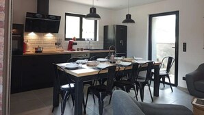Eine moderne Küche mit schwarzen Schränken, einem Esstisch und Stühlen. Über dem Tisch hängen Pendelleuchten.