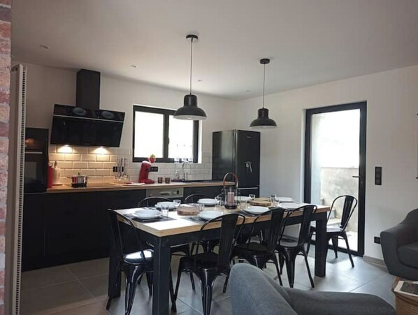 A modern kitchen with black cabinets, a dining table, and chairs. There are pendant lights above the table.