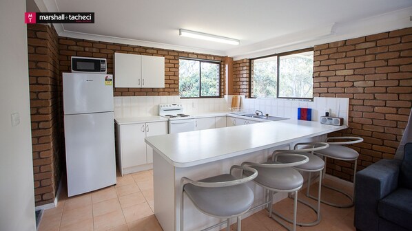 A compact kitchen with white cabinetry, a built-in microwave, a stove, and a large island with bar stools.