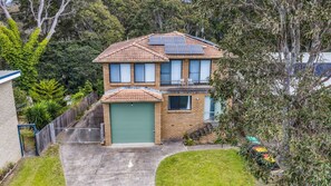 A two-story house with a green garage door, solar panels on the roof, and a fenced yard.