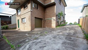 A two-story brick house with a garage door, a fenced yard, and a concrete driveway. - George Hideaway - George St 30A (Bermagui)