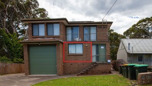 A two-story brick house with a green garage door, a balcony, and a small front yard. - George Hideaway - George St 30A (Bermagui)