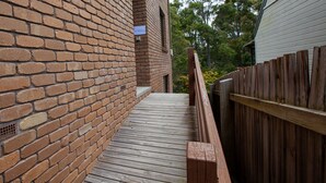 A brick exterior wall with a wooden deck leading to a wooden fence. - George Hideaway - George St 30A (Bermagui)