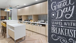 A modern kitchen with wooden cabinets, a white island with bar stools, pendant lighting, and a chalkboard with motivational writing.