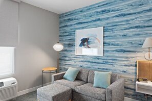 A modern living room with a grey sectional sofa, a framed abstract painting, a floor lamp, and a small table. - Towneplace Suites By Marriott White Hall (White Hall)