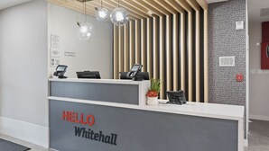 A reception desk with a "HELLO Whitehall" sign, a plant, and a modern light fixture.