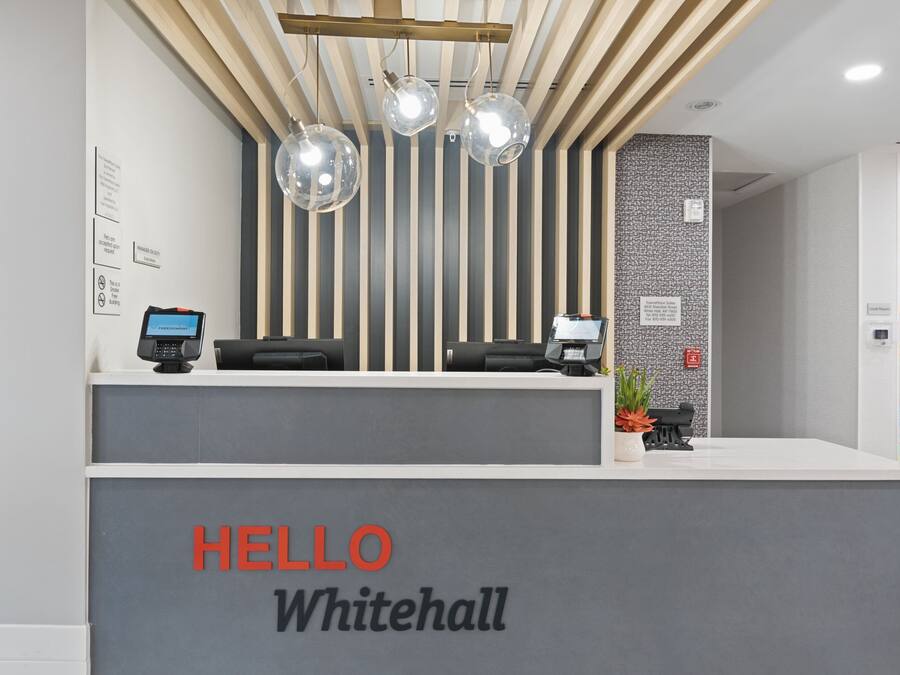 A reception desk with a 'HELLO Whitehall' sign, a modern light fixture, and a security camera.