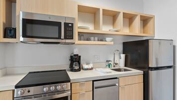 A modern kitchen with a built-in microwave, stove, and dishwasher. There are wooden cabinets and a countertop with a coffee maker and cups.