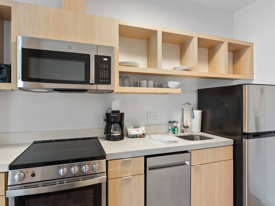 A modern kitchen with a built-in microwave, stove, and dishwasher. There are wooden cabinets and a countertop with a coffee maker and cups.