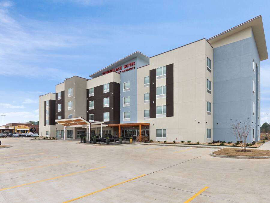 A modern hotel with a flat roof, multiple floors, and a large parking lot.